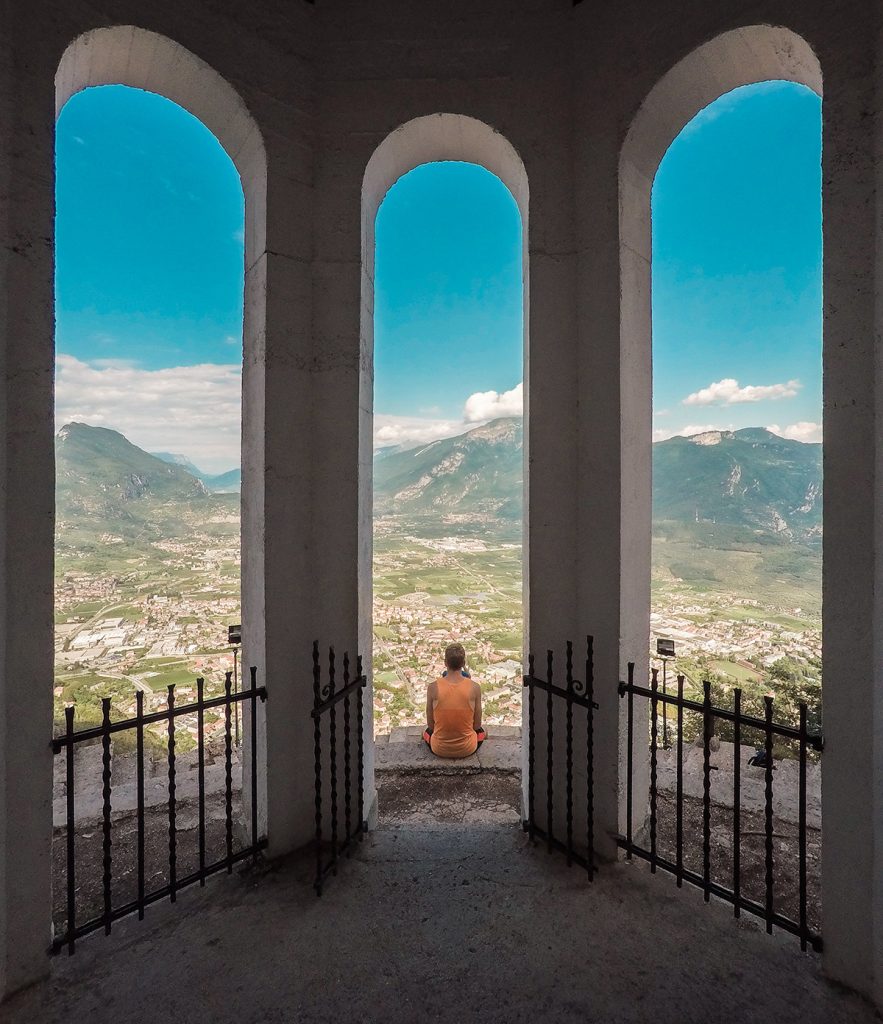 Eine Person sitzt auf einer Aussichtsplattform mit Blick auf Riva del Garda am Gardasee.