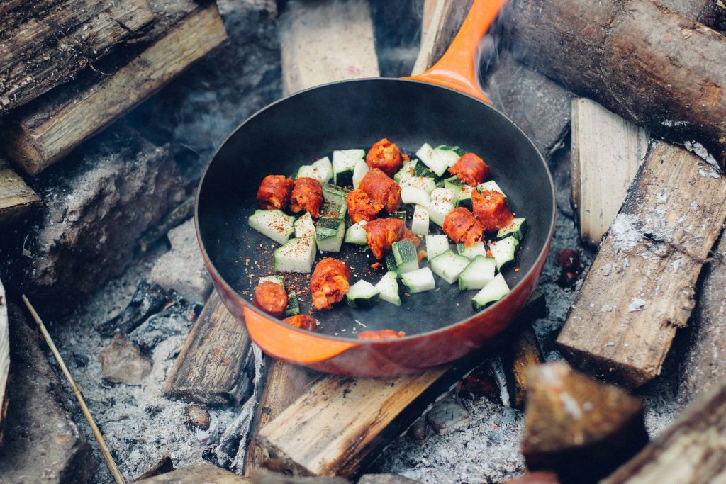 Pfanne, die mit verschiedenem Gemüse gefüllt auf einem Lagerfeuer steht.