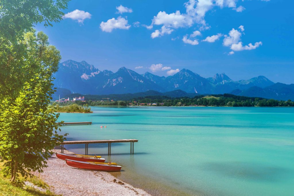 Ein Ufer des Forggensees mit Gipfelketten im Hintergrund.