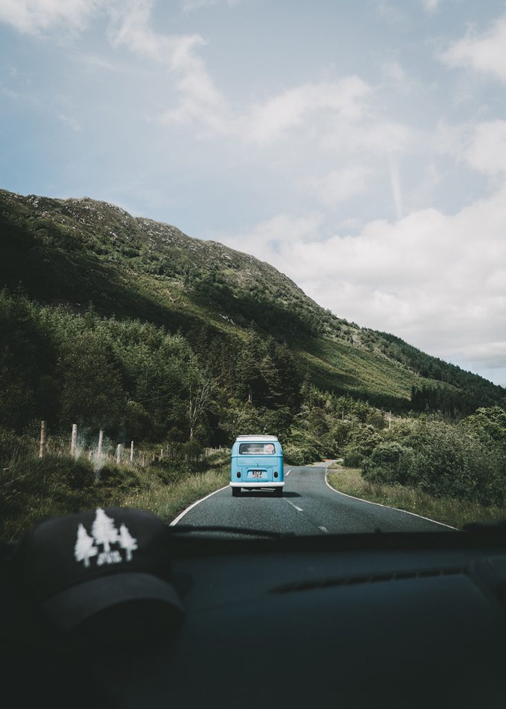 Ein blauer Camper fährt auf einer Straße, die durch bergige Landschaft fährt.