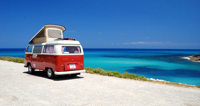 Ein roter Camper parkt mit Blick über das blaue Meer.