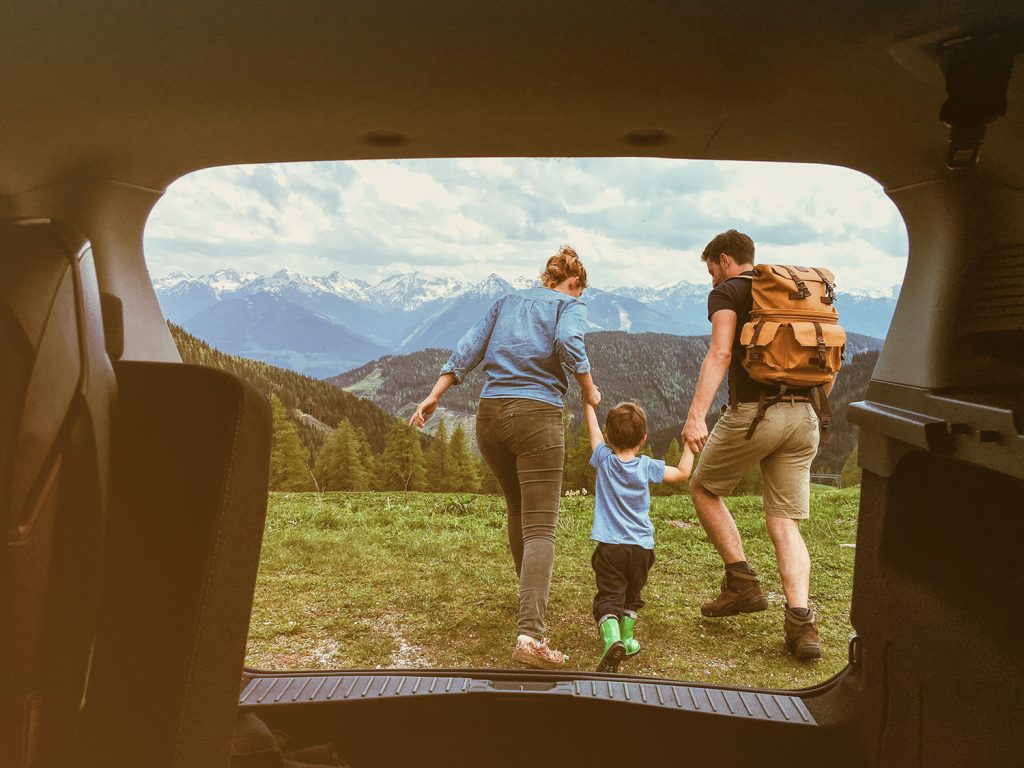 Eine junge Familie auf einer Wiese mit schneebedeckten Bergen im Hintergrund.