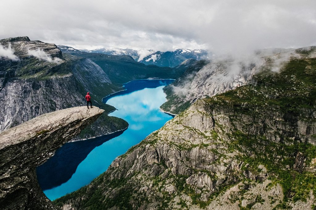 Eine Person steht am Rand einer Klippe über einem Fjord. Eine Person steht am Rand einer Klippe über einem Fjord.
