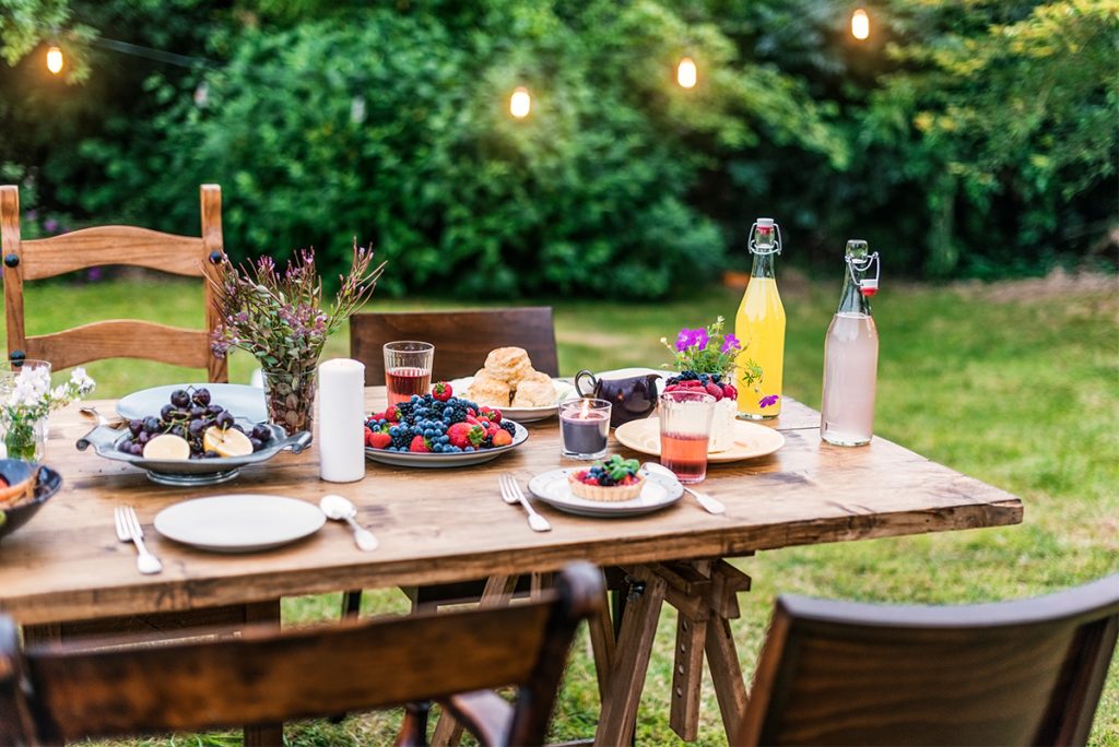 Ein mit Obst und Gebäck gedeckter Holztisch und Stühle in einem Garten. Ein mit Obst und Gebäck gedeckter Holztisch und Stühle in einem Garten.