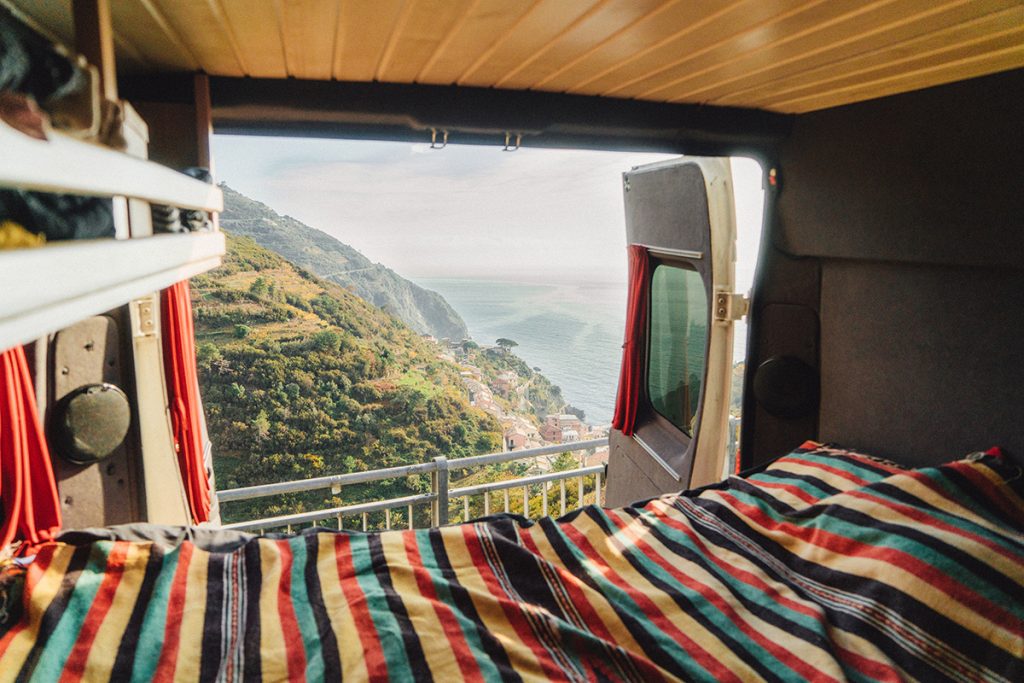 Durch die offene Heckklappe eines Campers ist bergige Landschaft an der Küste zu sehen. Durch die offene Heckklappe eines Campers ist bergige Landschaft an der Küste zu sehen.