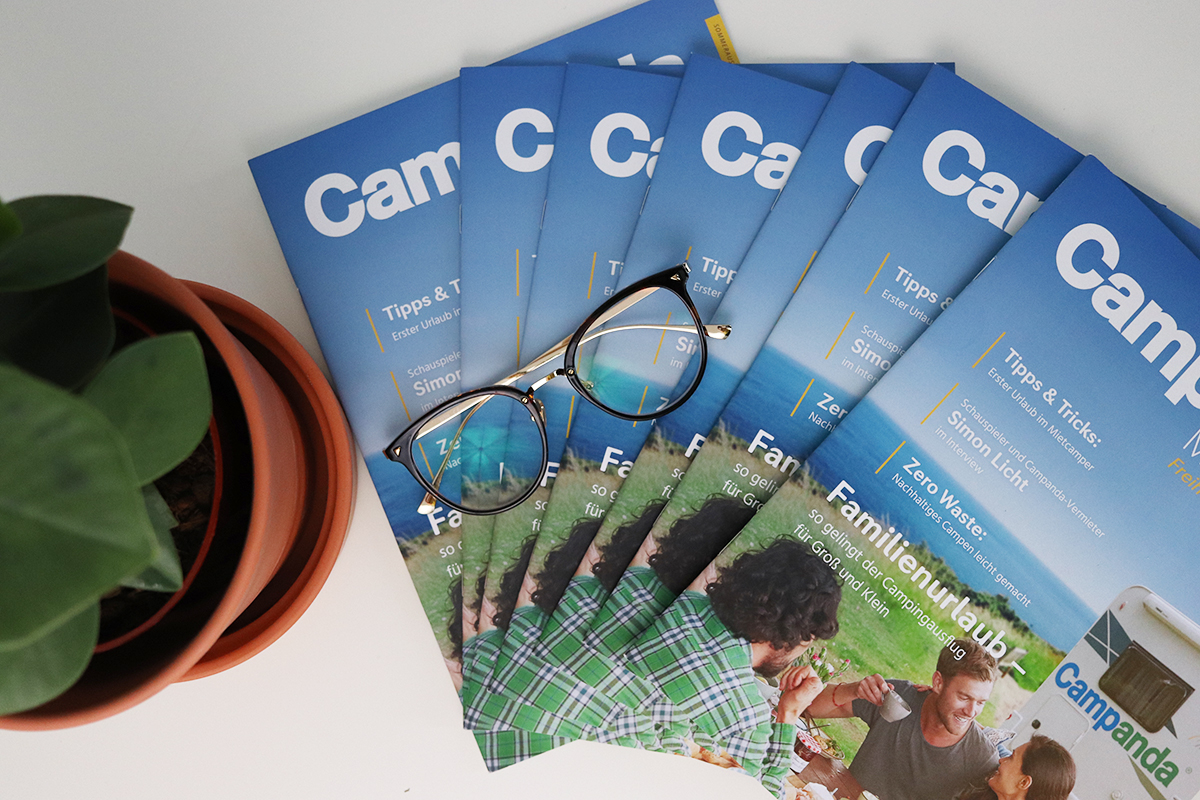 Das erste Campanda Kundenmagazin Print Magazine aufgefächert, mit Pflanze und Brille als Dekoration.