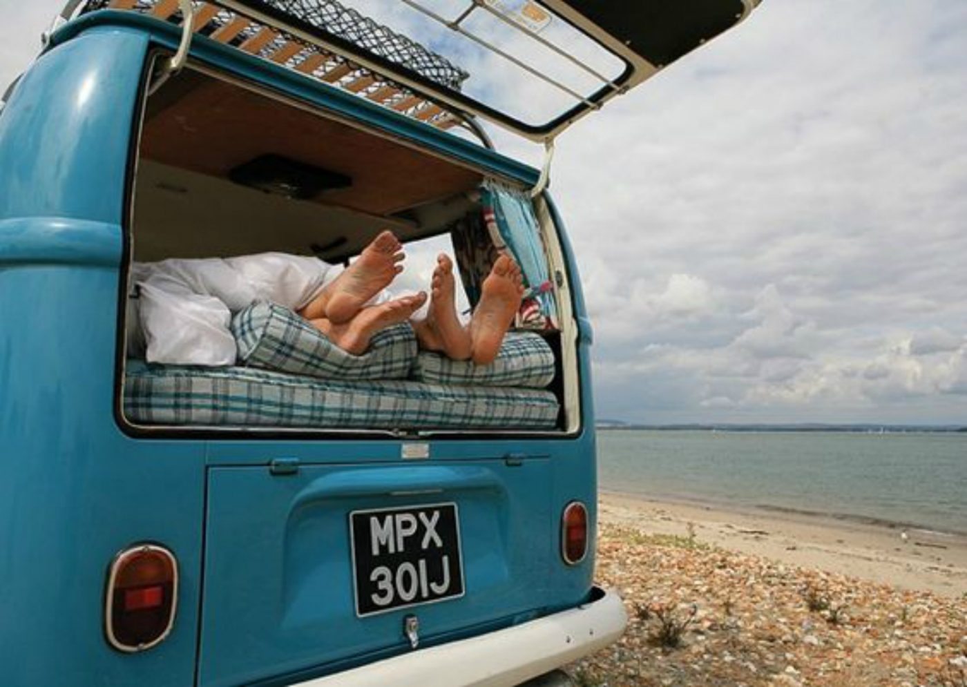 Zwei Paar Füße gucken aus der offenen Heckklappe eines Retro-Campervans.