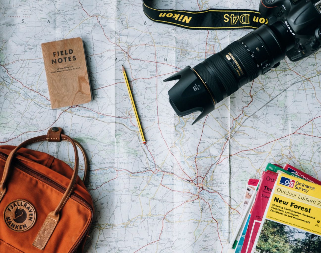 Rucksack, Kamera, Notizheft und Straßenkarten liegen auf einer ausgebreiteten Karte.