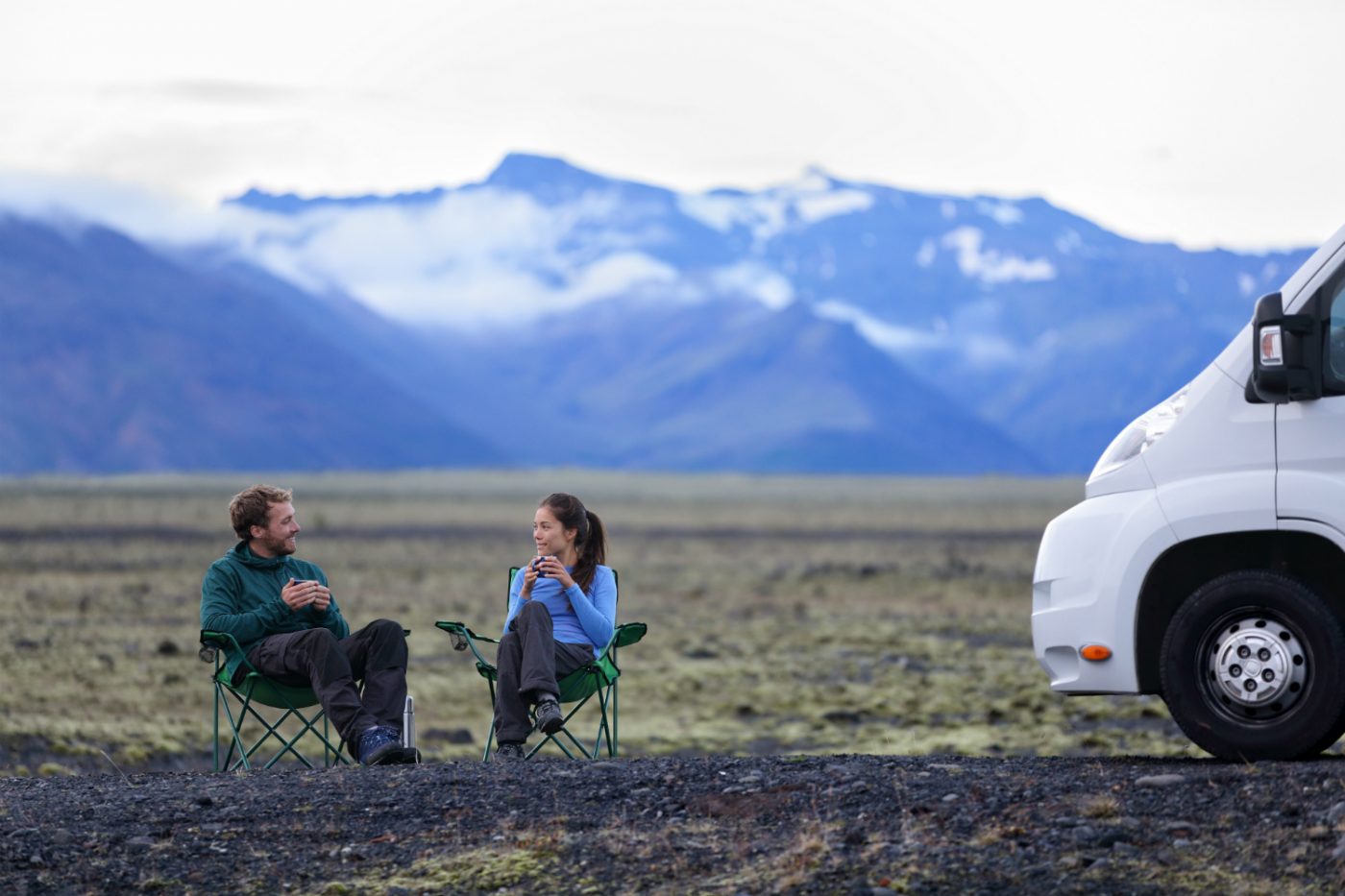 Ein Paar sitzt auf Campingstühlen neben einem Wohnmobil inmitten der Landschaft Islands.