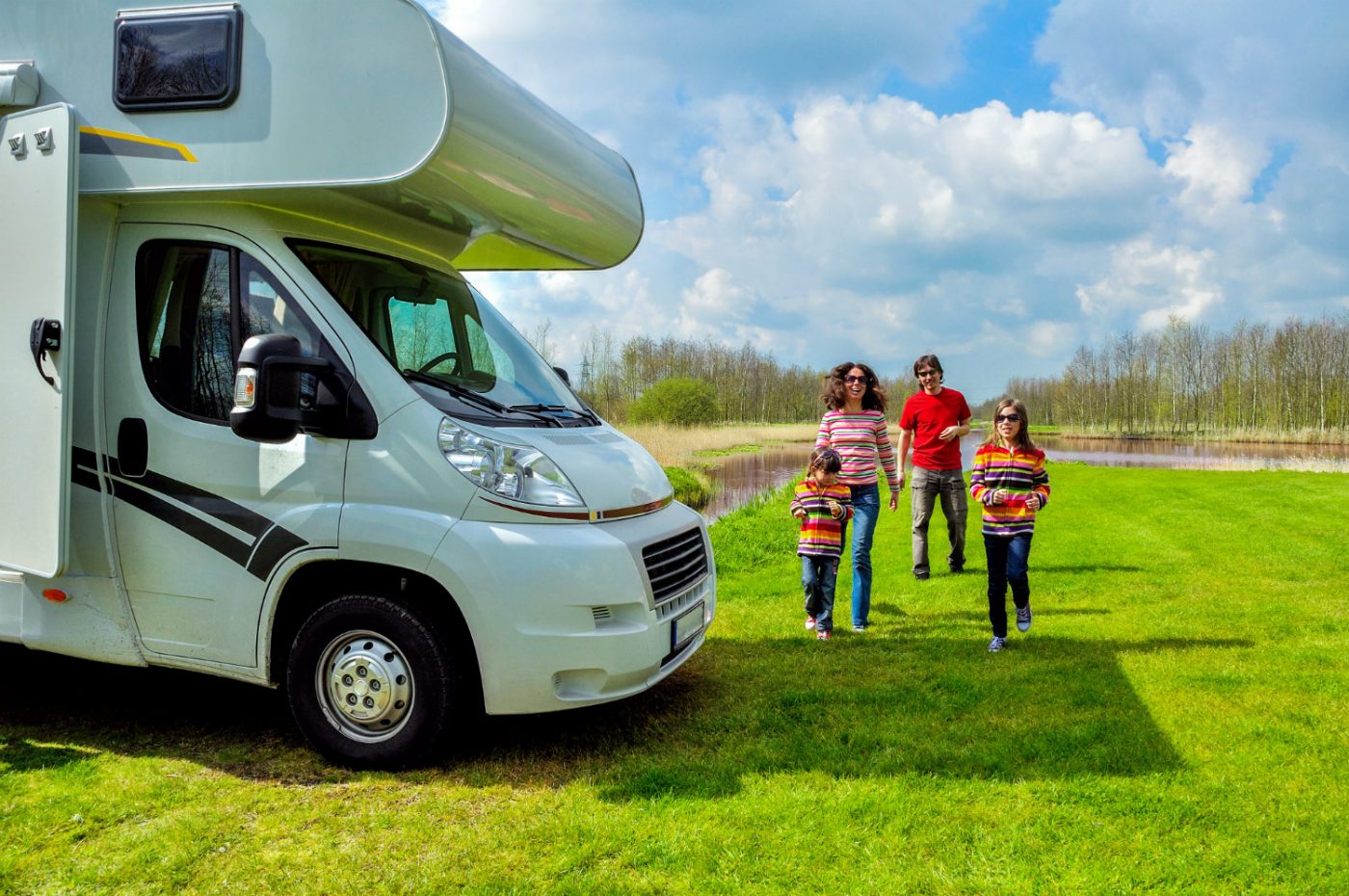 Eltern mit zwei Kindern auf einer Wiese neben einem Wohnmobil.