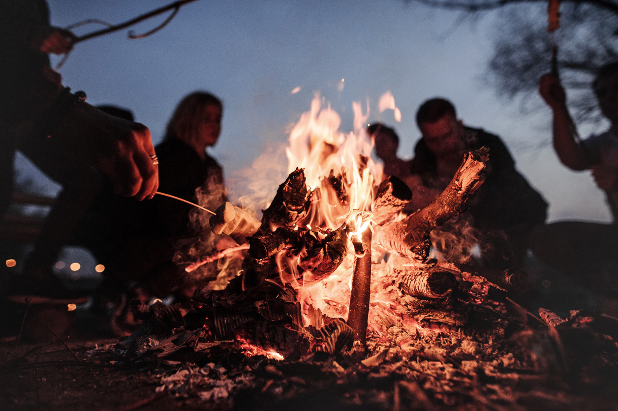 Gemeinsame Zeit als Familie ist beim Urlaub im Wohnmobil besonders wichtig. Eine Gruppe von Menschen sitzt um ein Lagerfeuer herum.