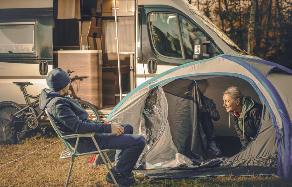 Vor allem beim Urlaub mit Teenagern ist Rückzugsraum wichtig. Zum Beispiel in Form eines kleinen Zeltes neben dem Wohnmobil. Drei Menschen bauen ein kleines Zelt auf. Im Hintergrund ist ein Wohnmobil zu sehen.