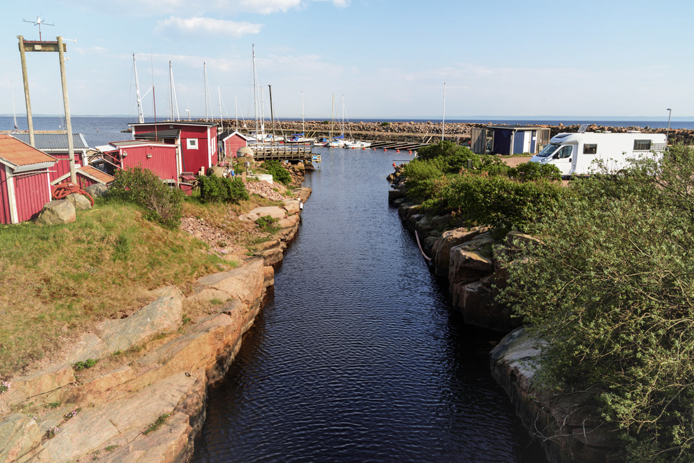 Rote, schwedische Häuser und ein Wohnmobil sind am Wasser zu sehen.