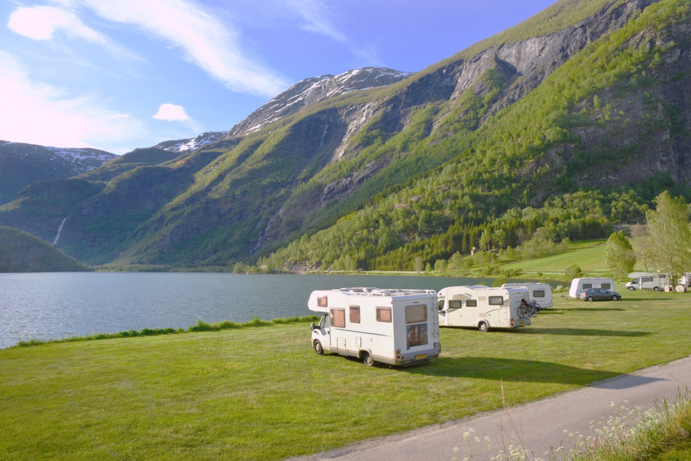 Einige Wohnmobile auf Stellplätzen am See vor Alpenkulisse in Bayern.