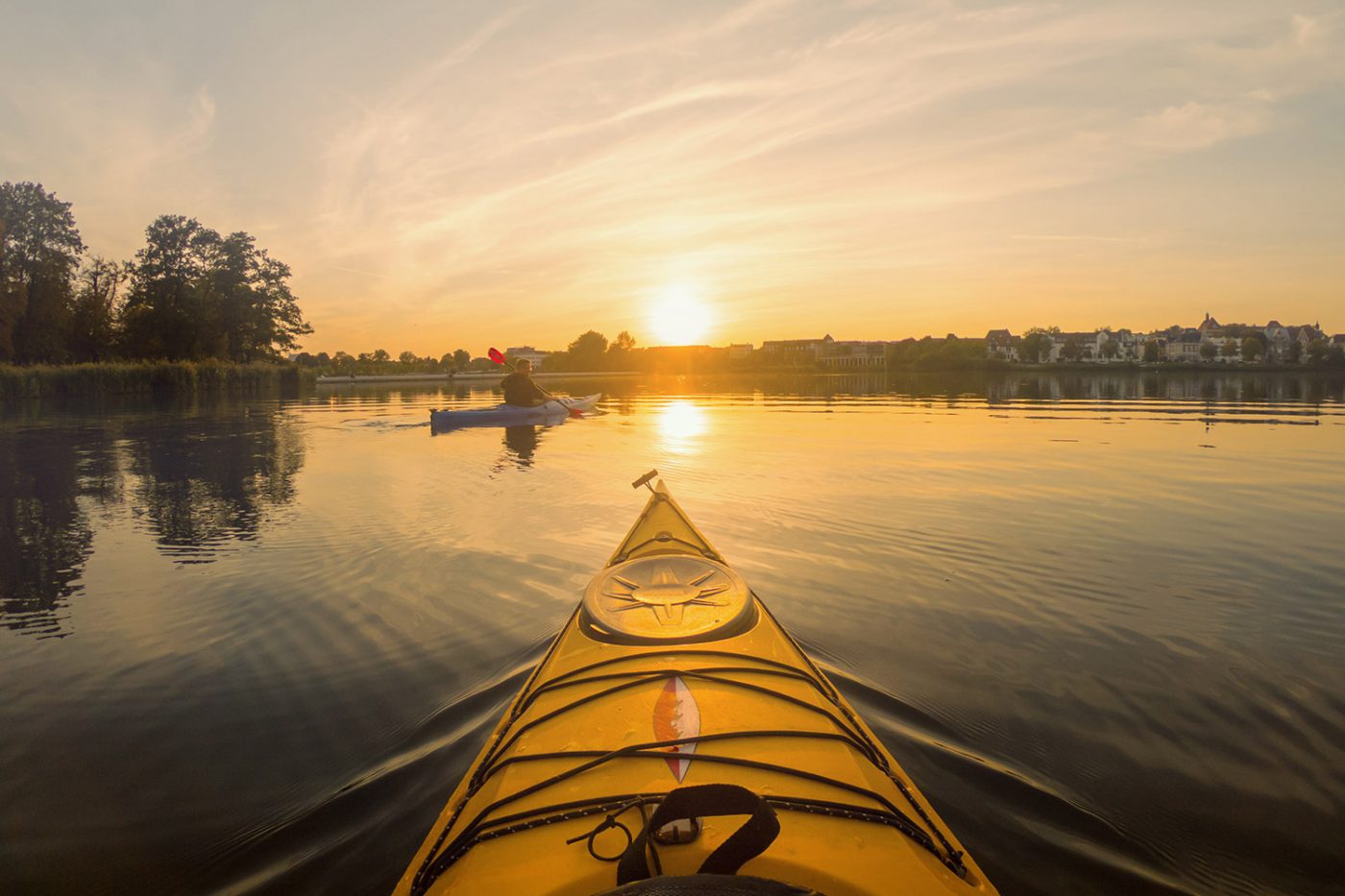 Ein Kajak bei Sonnenuntergang und ein Paddler im Hintergrund.