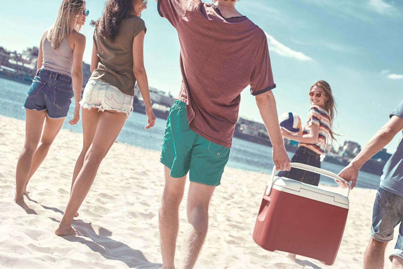 Junge Menschen am Strand tragen eine Kühlbox.