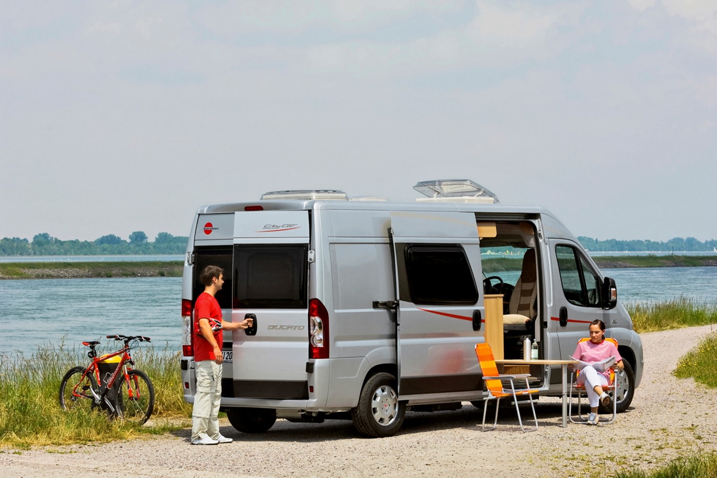 Zwei Campingreisende mit Kastenwagen machen Pause am Fluss