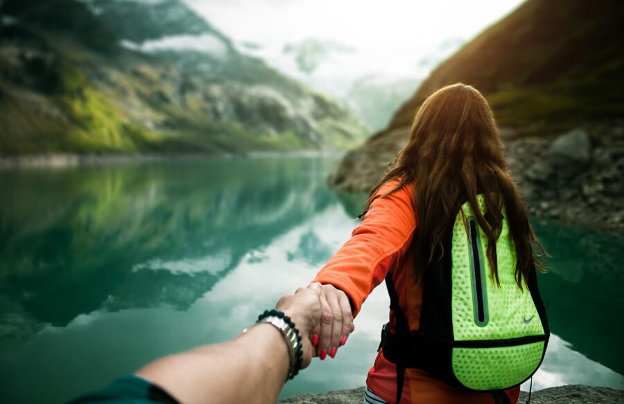 Junge Frau mit grünem Rucksack an Bergsee nimmt Mann an der Hand
